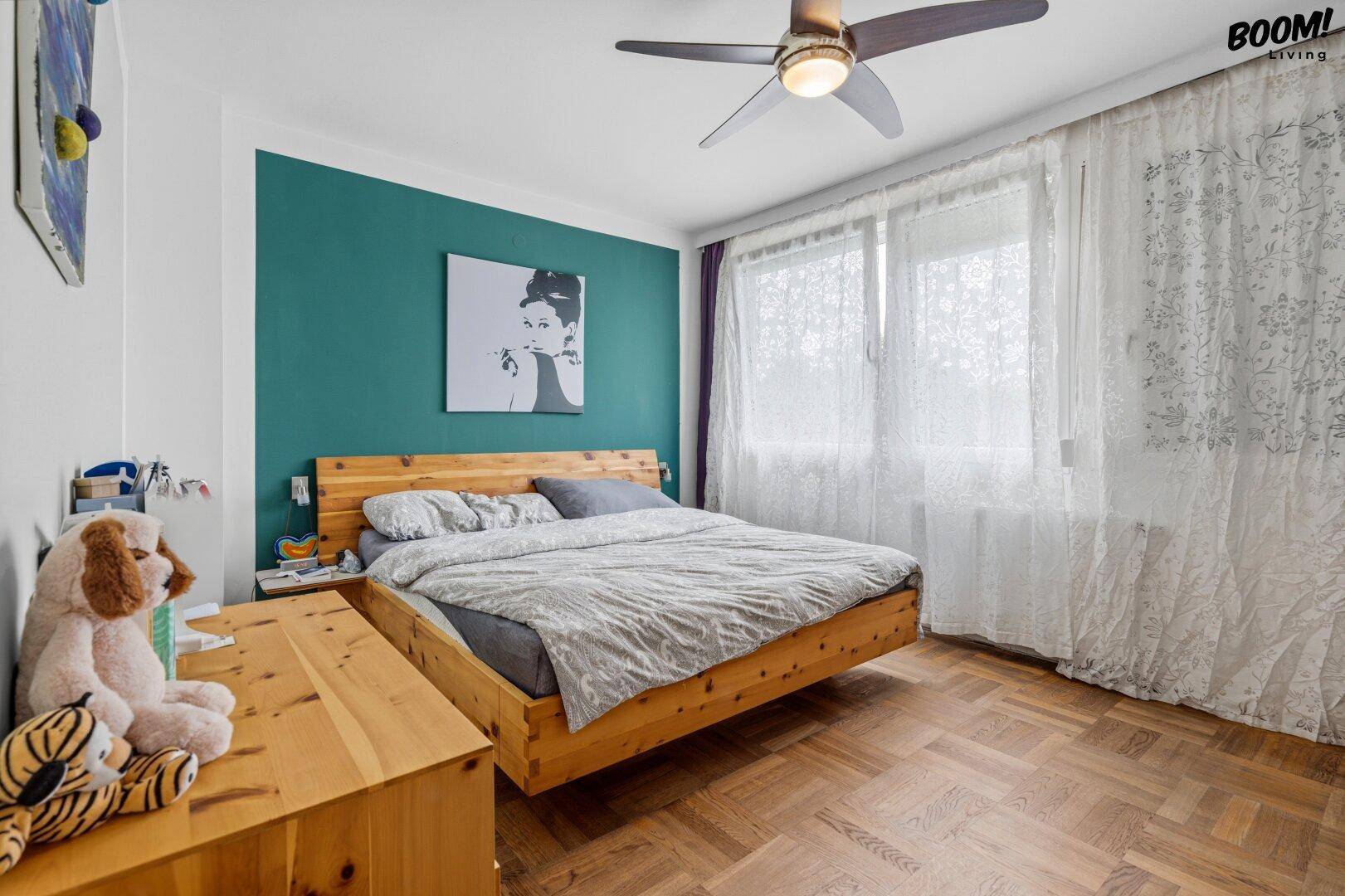 Helles Schlafzimmer mit Holzboden, großem Bett und farbiger Akzentwand.