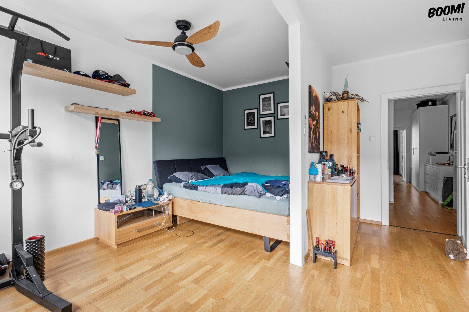 Schlafzimmer mit Holzboden, Deckenventilator und einer dunkelgrünen Akzentwand, hell und geräumig.