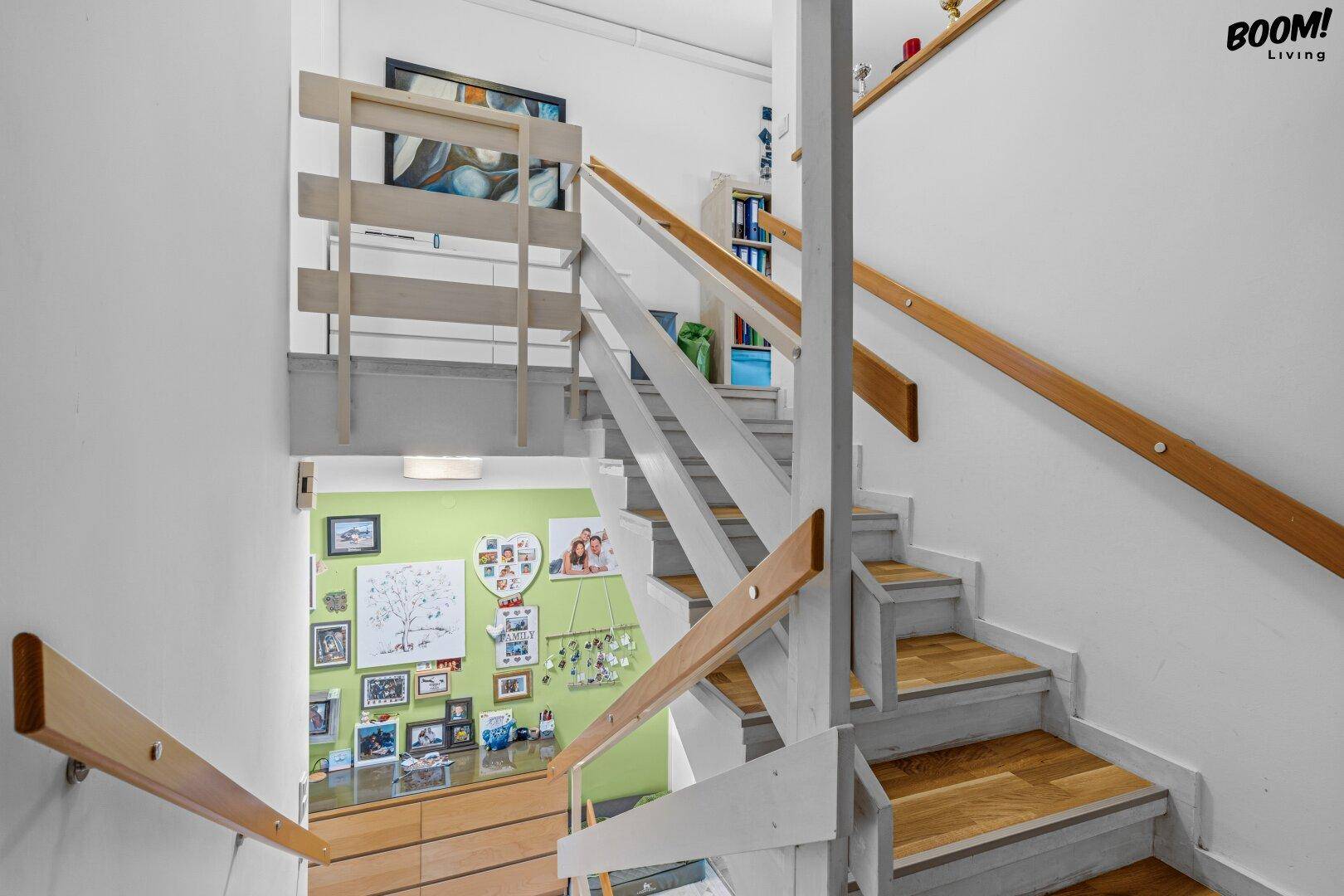 Treppenhaus mit Holzstufen und weißem Geländer, das die verschiedenen Ebenen verbindet.