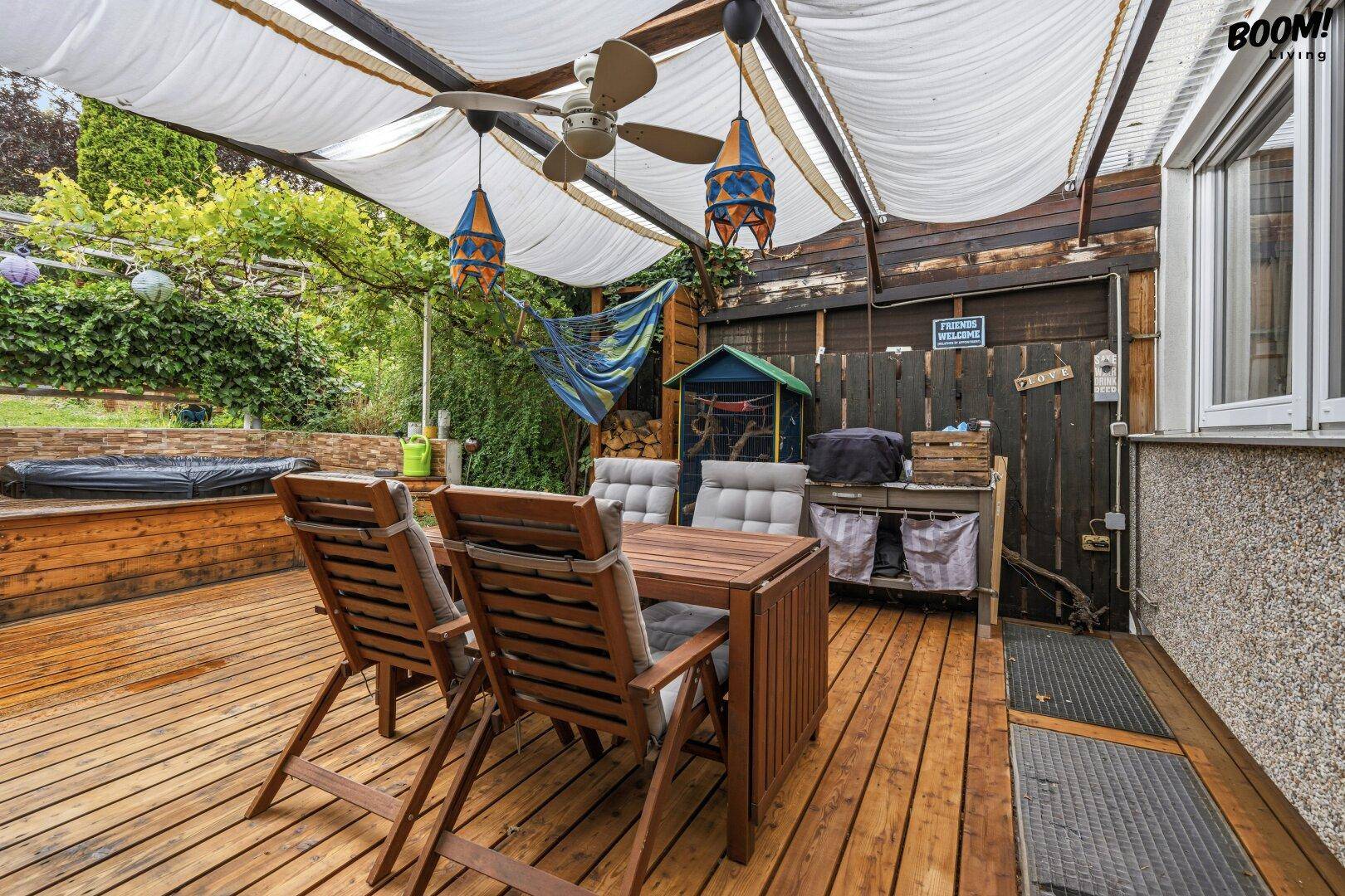 Überdachte Holzterrasse mit Essbereich, Hängematte und Whirlpool im Hintergrund, ideal zum Entspannen.