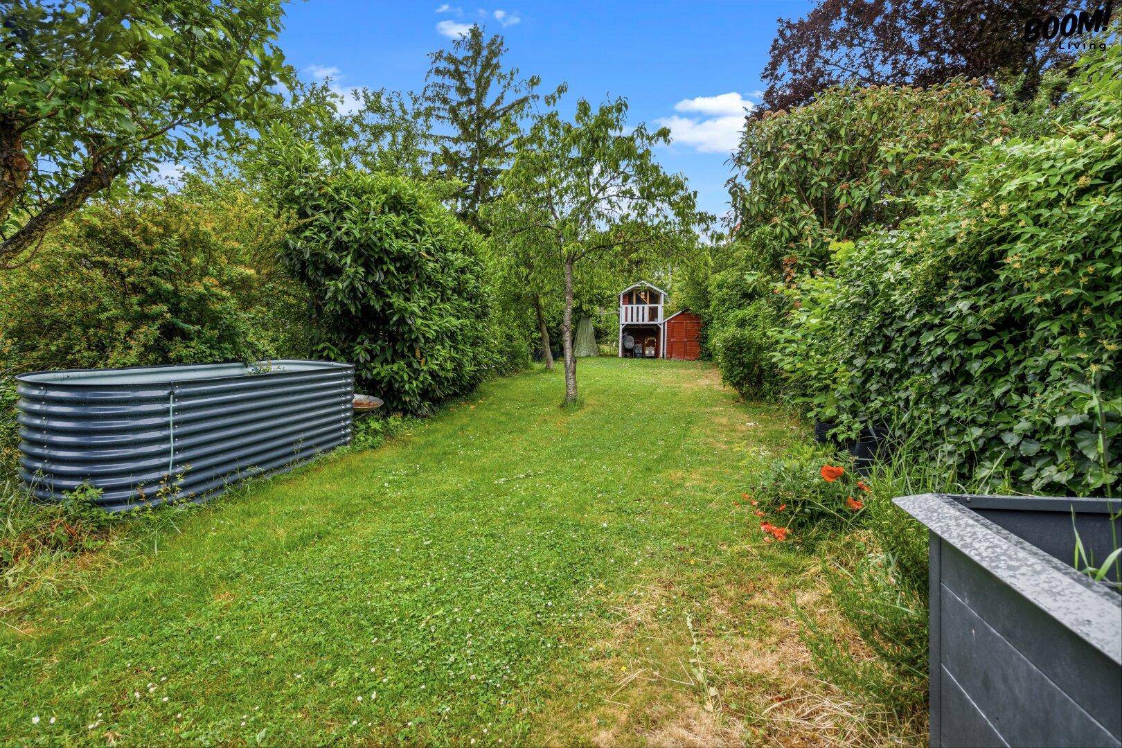 Grüner Garten mit Rasenfläche, Bäumen und einem Gartenhaus im Hintergrund, bietet viel Platz.