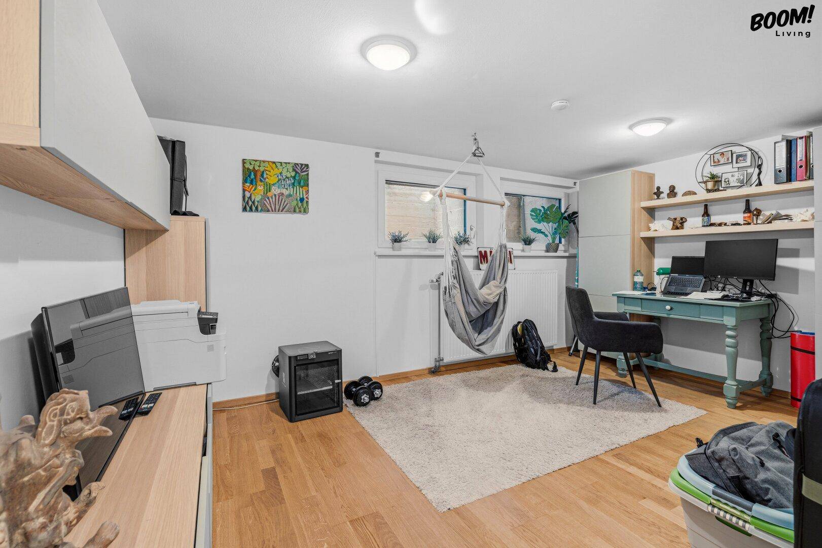 Helles Zimmer mit Holzfußboden, Schreibtisch und Hängesessel, vielseitig nutzbar als Schlaf- oder Arbeitszimmer.