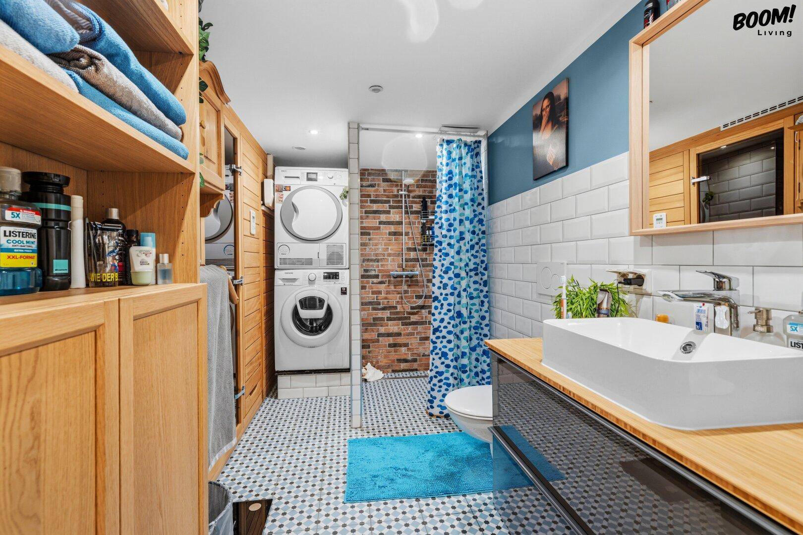 Funktionales Badezimmer mit Dusche, WC, Waschbecken und integriertem Waschmaschinen-Trockner-Turm.