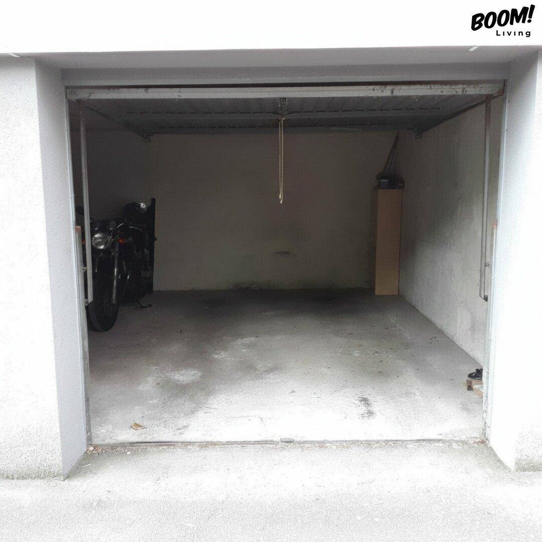 Leere Garage mit Betonboden und einem Motorrad im hinteren Bereich.