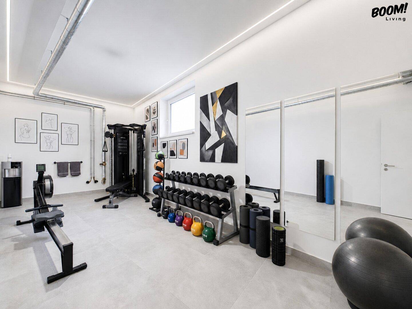 Gut ausgestatteter Fitnessraum mit verschiedenen Trainingsgeräten und Spiegelflächen.