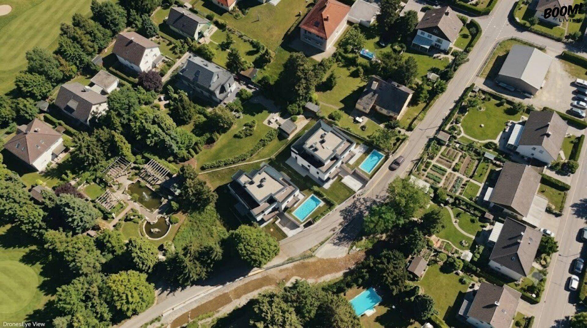 Luftaufnahme einer modernen Wohnanlage mit Pools und Gärten in grüner Umgebung.