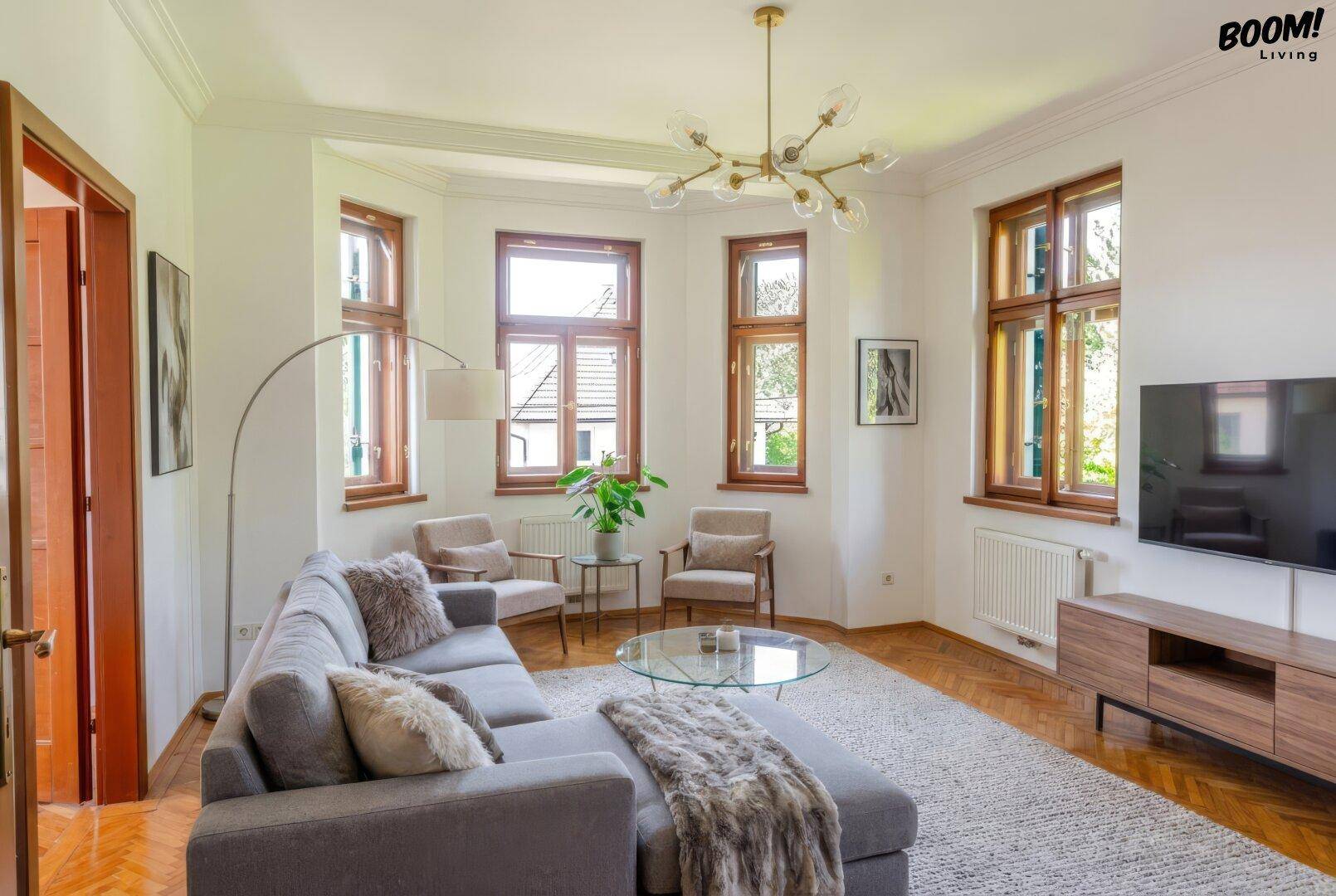 Helles Wohnzimmer mit Parkettboden, großen Fenstern und moderner Einrichtung in neutralen Tönen.