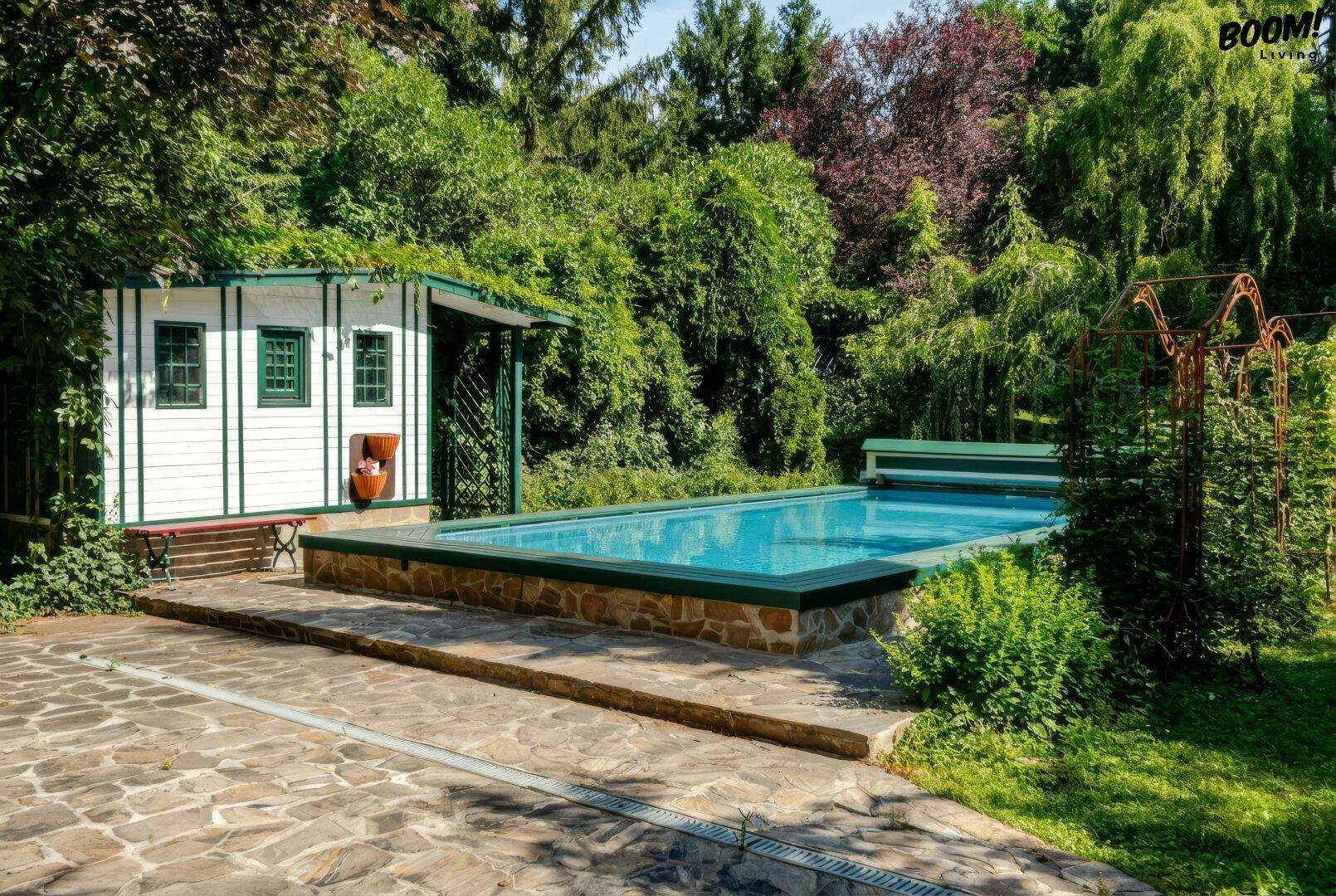 Außenbereich mit Pool, kleinem Gartenhaus und üppiger grüner Vegetation.