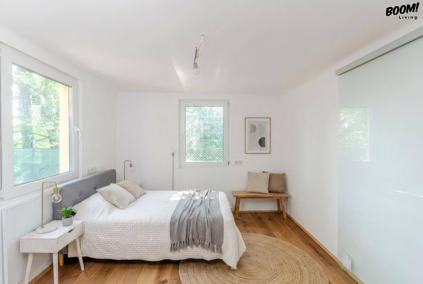 Helles Schlafzimmer mit Holzboden, großen Fenstern und minimalistischer Einrichtung.