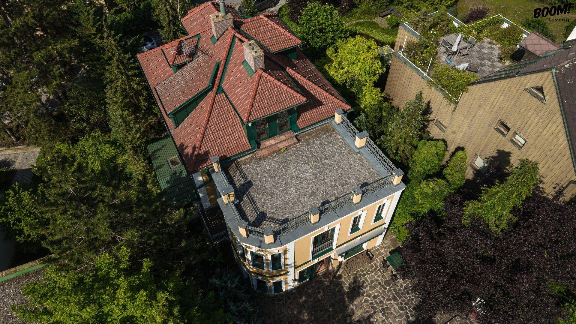 Vogelperspektive der Villa mit großem Dach und umliegenden Bäumen in sonniger Umgebung.