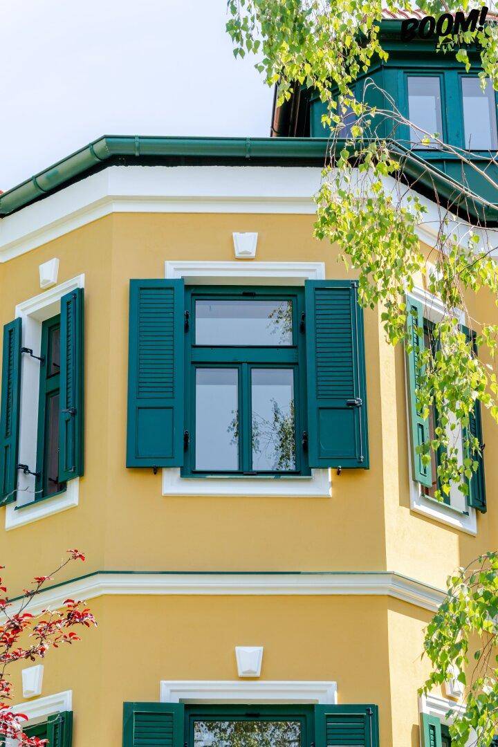 Detailansicht der gelben Fassade mit grünen Fensterläden und Fenstern.