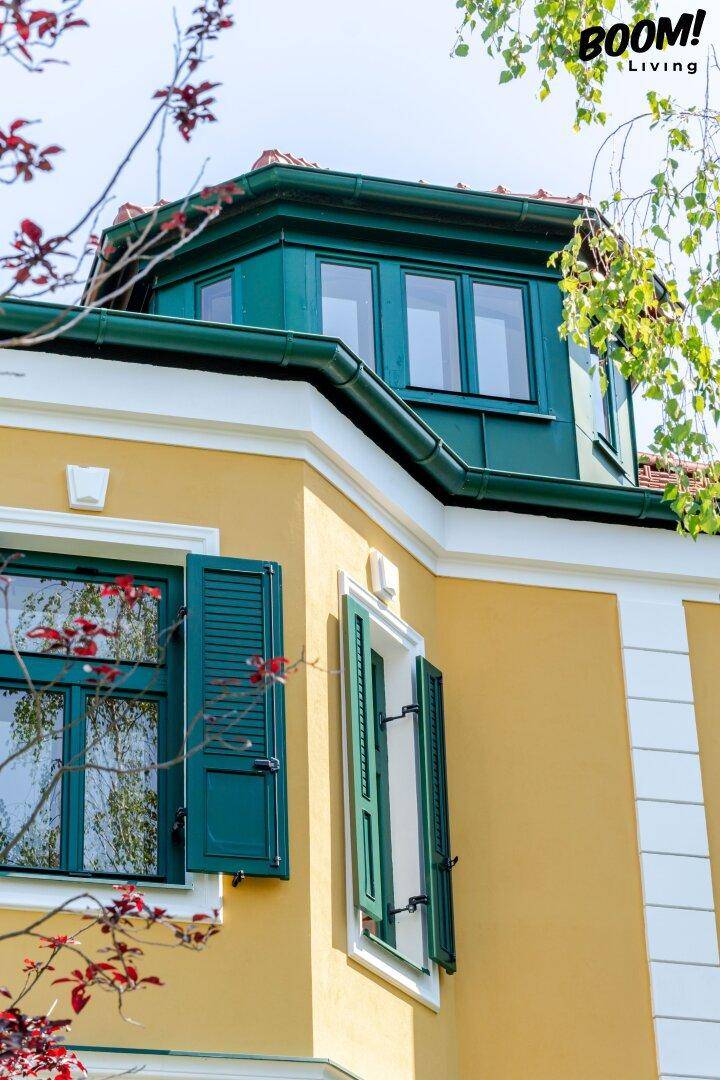 Detailansicht der oberen Etage der Villa mit grünen Fensterläden und Dach.