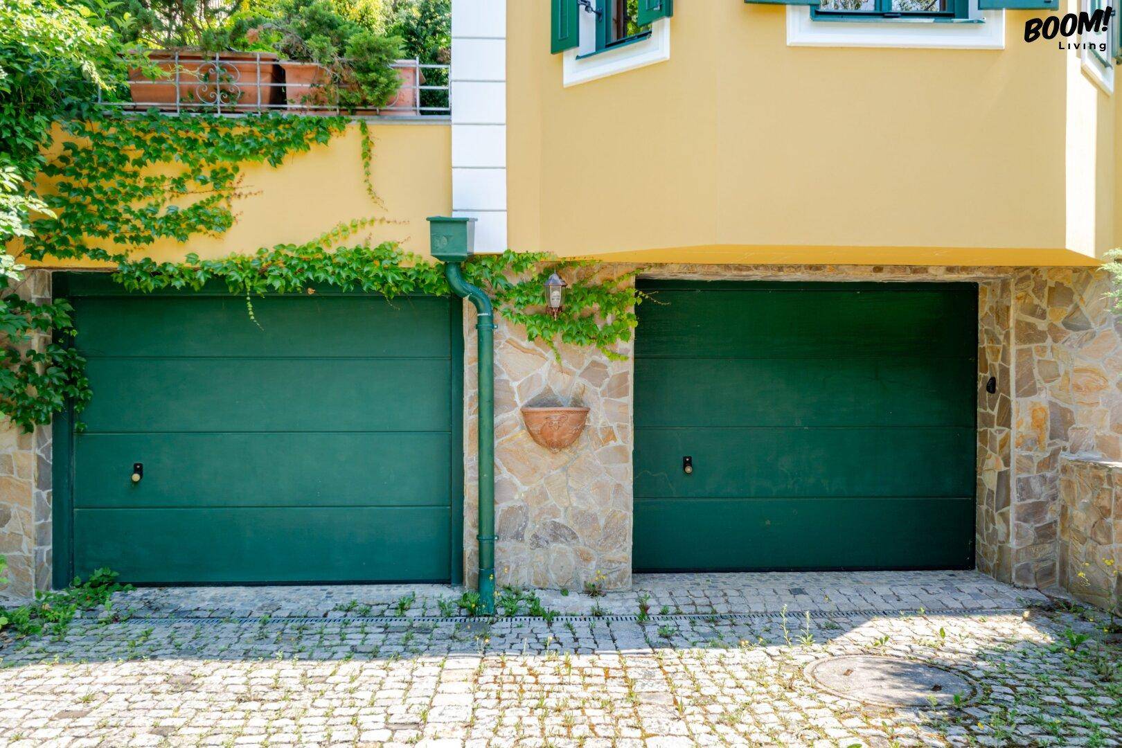 Geschlossene grüne Garagentore mit Steinfassade unterhalb der Villa.