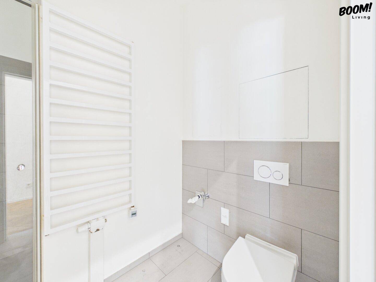 Modernes WC mit Wand-WC, grauen Fliesen und beheiztem Handtuchhalter.