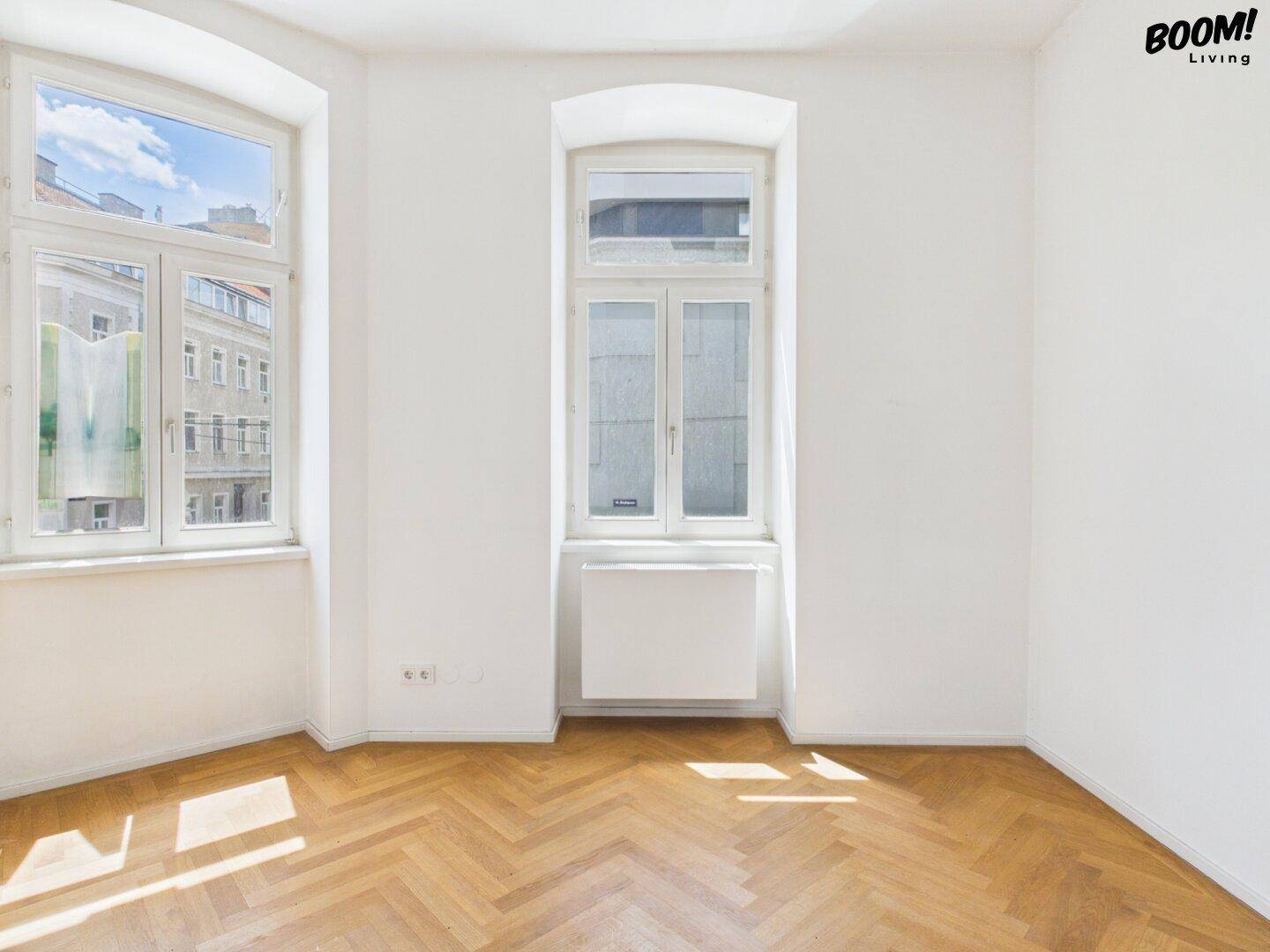 Geräumiger, heller Raum mit Fischgrätparkett und hohen Fenstern, ideal für individuelle Gestaltung.