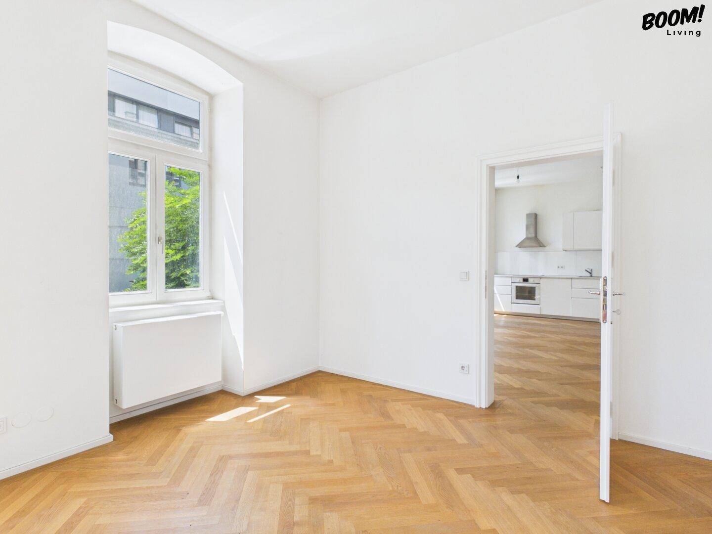 Heller Raum mit Fischgrätparkett und Zugang zur Küche, ideal für offenes Wohnen.