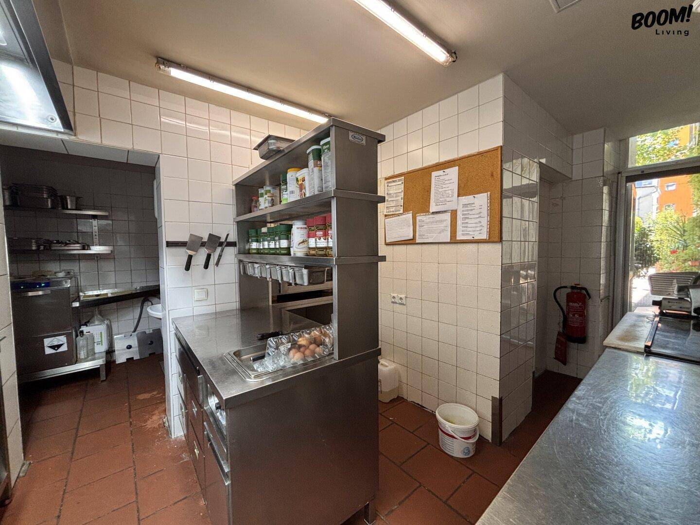 Geräumige Gewerbeküche mit Edelstahlmöbeln, weißen Fliesenwänden und Terrakotta-Boden.
