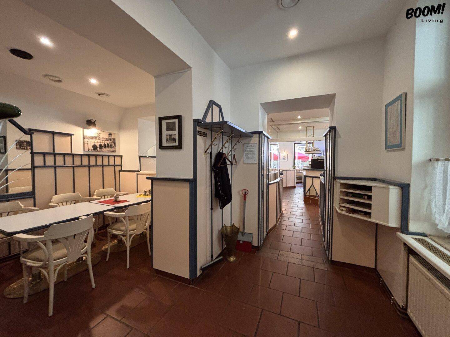 Eingangsbereich eines Gastraums mit Garderobe, Tischen und einem Durchgang zu weiteren Bereichen.