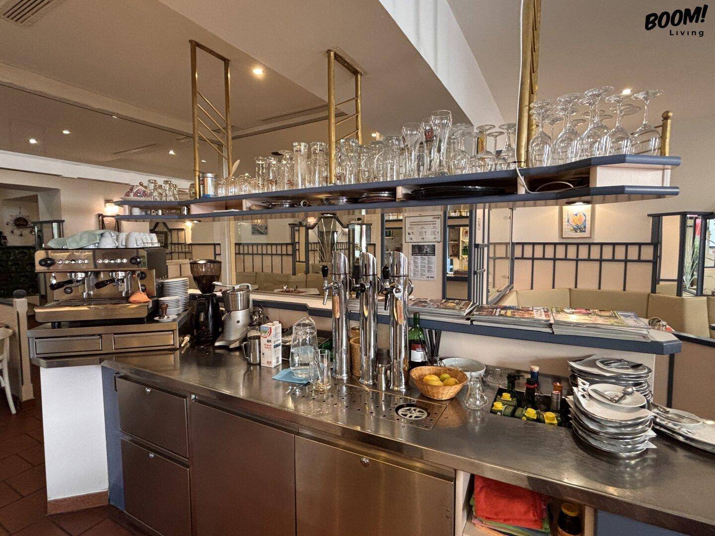 Bar-Bereich mit Zapfanlage, Kaffeemaschine und vielen Gläsern auf einem Regal über der Theke.
