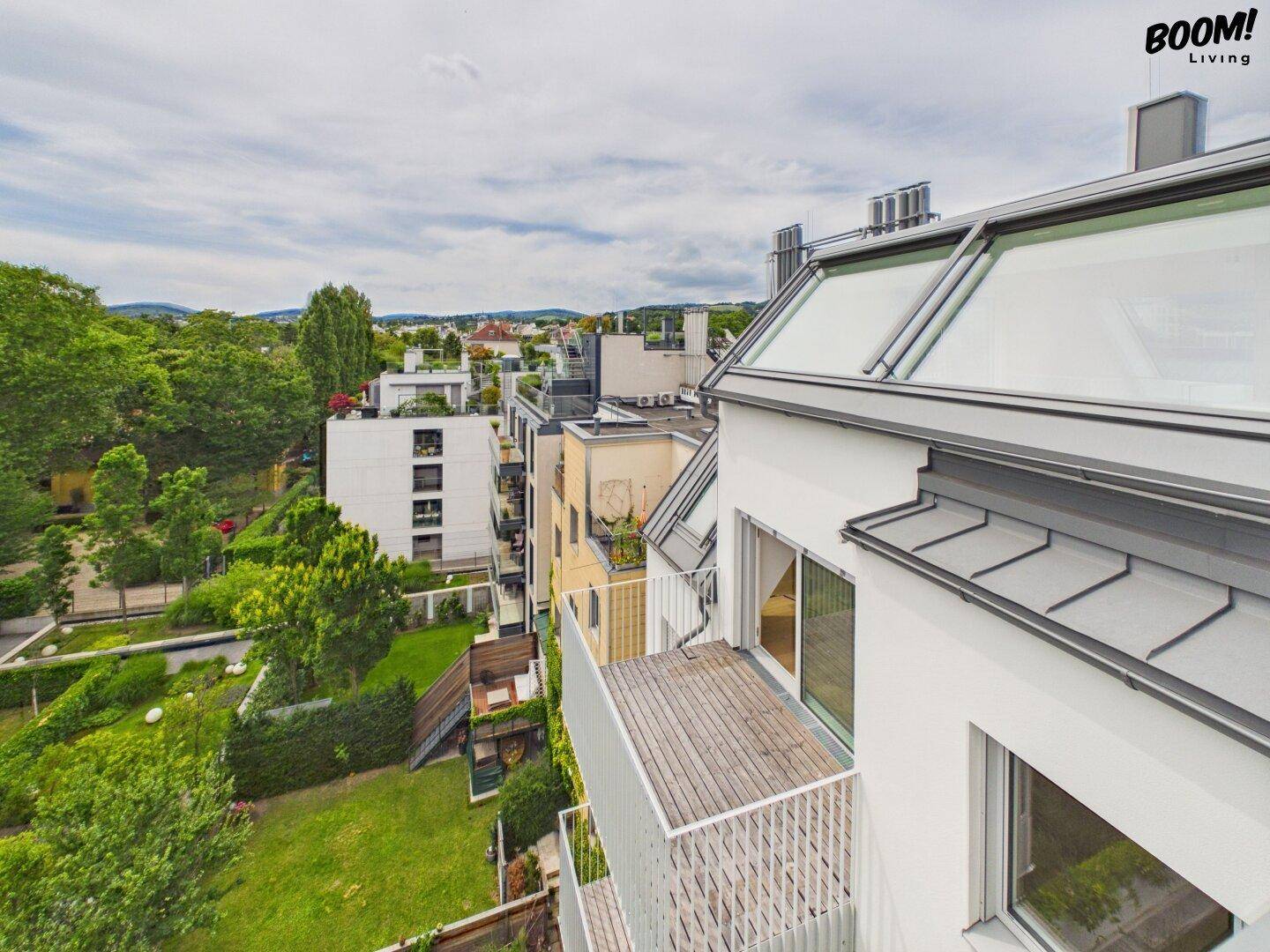 Balkon mit Holzboden und Blick auf die grüne Umgebung und weitere Gebäude.