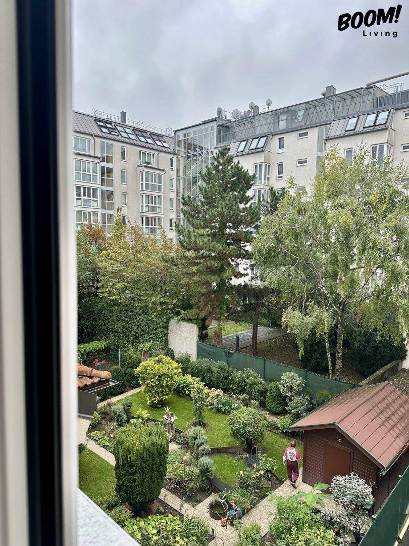 Blick aus dem Fenster auf einen gepflegten Innenhofgarten mit Bäumen und einem kleinen Gartenhaus.