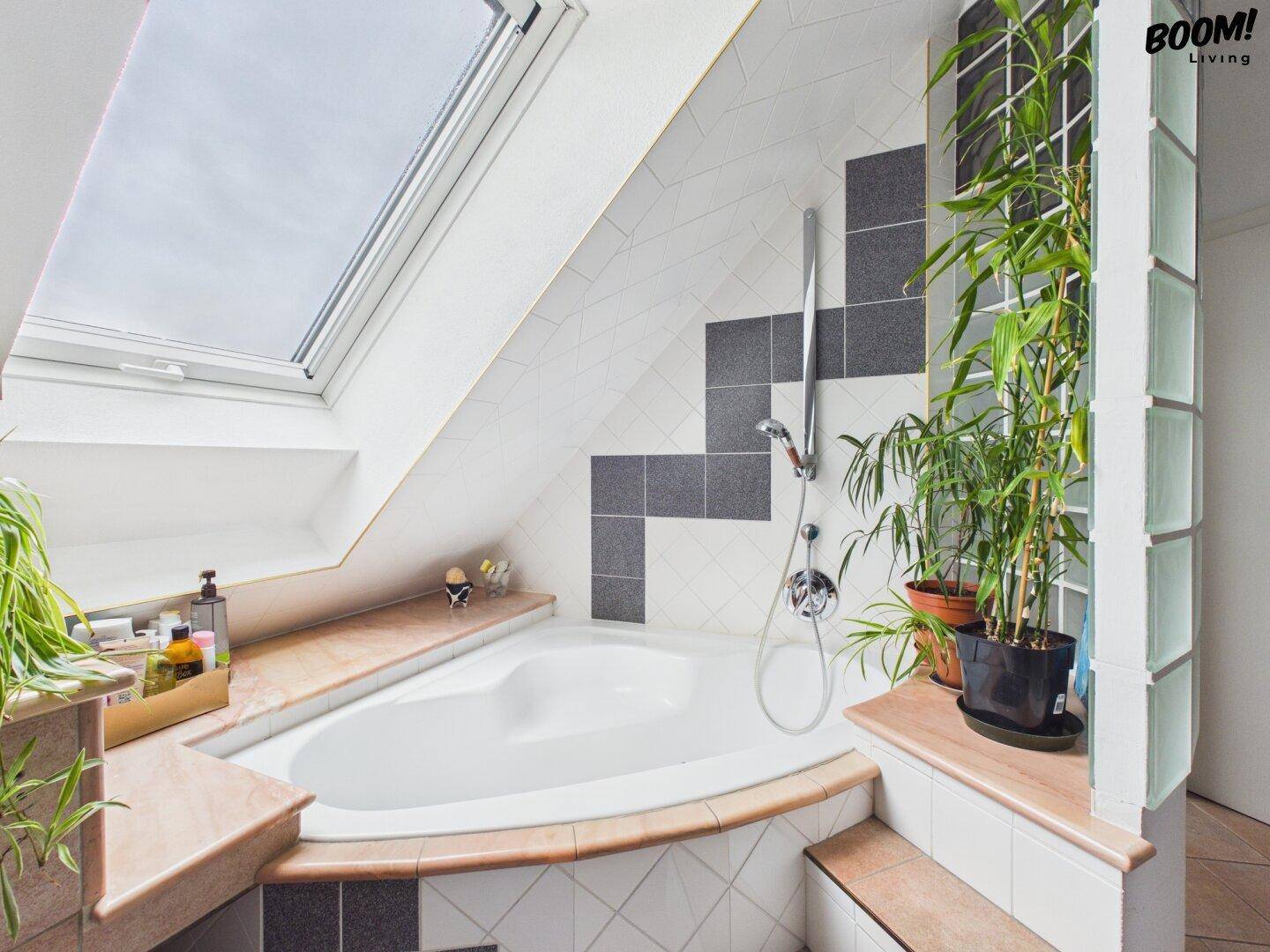 Badezimmer im Dachgeschoss mit Eckbadewanne, Dachfenster und dekorativen Pflanzen.