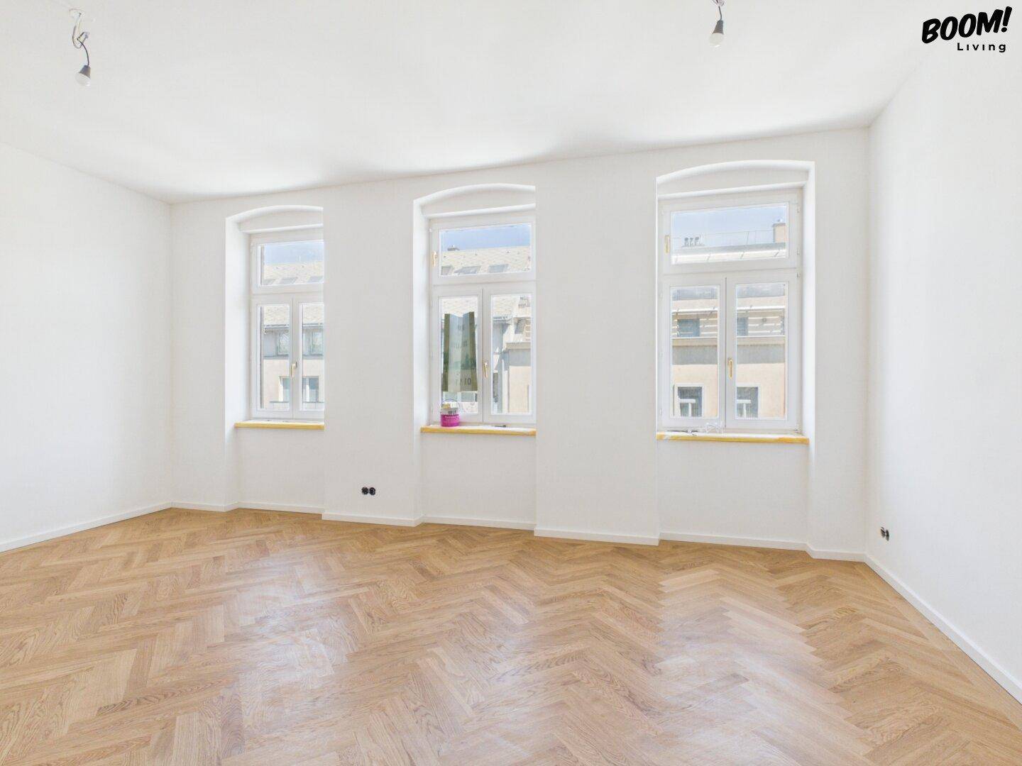 Heller, leerer Raum mit Fischgrätparkett und drei großen Fenstern, bereit zur individuellen Gestaltung.