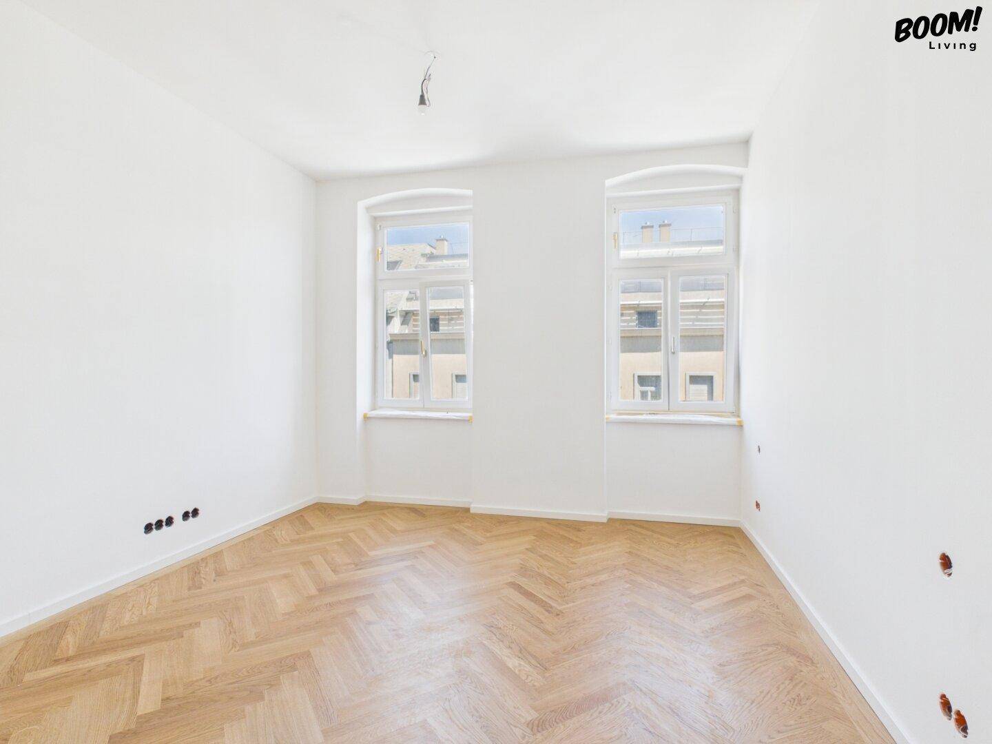 Leerer, heller Raum mit Fischgrätparkett und zwei Fenstern, ideal für Schlaf- oder Arbeitszimmer.
