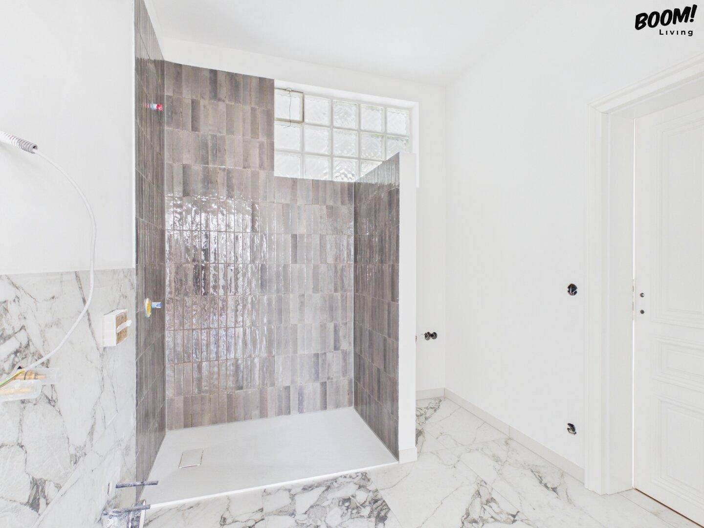 Modernes Badezimmer im Bau mit begehbarer Dusche, Marmorfliesen und Glasbausteinfenster.