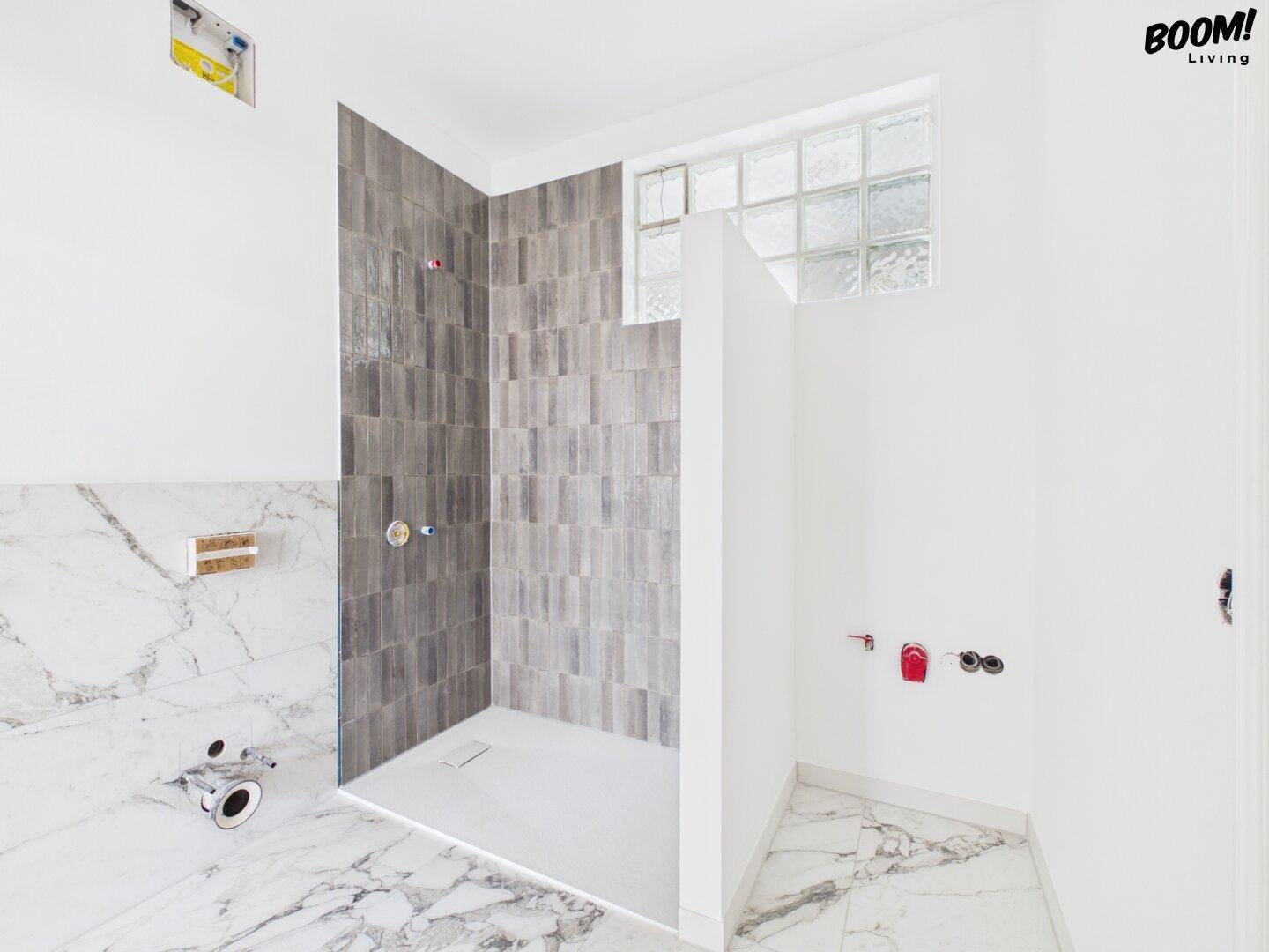 Badezimmer im Bau mit begehbarer Dusche, Marmorfliesen und Vorbereitung für Sanitärinstallationen.