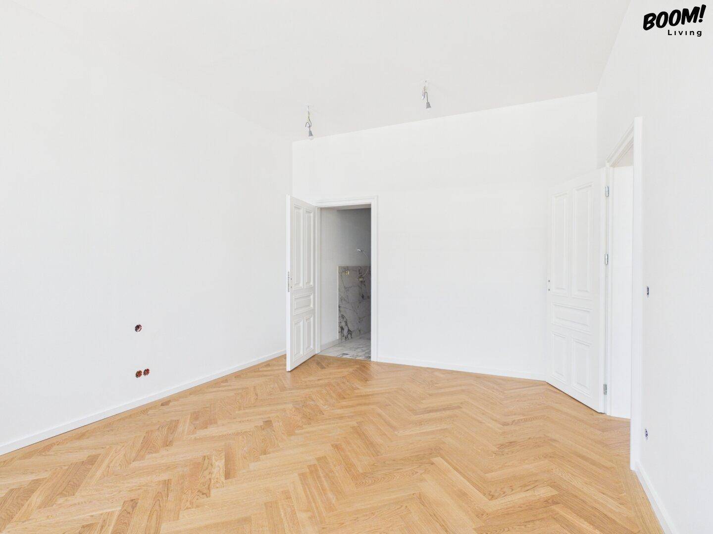 Heller, leerer Raum mit Fischgrätparkett und offenen Türen, bereit für die Fertigstellung.