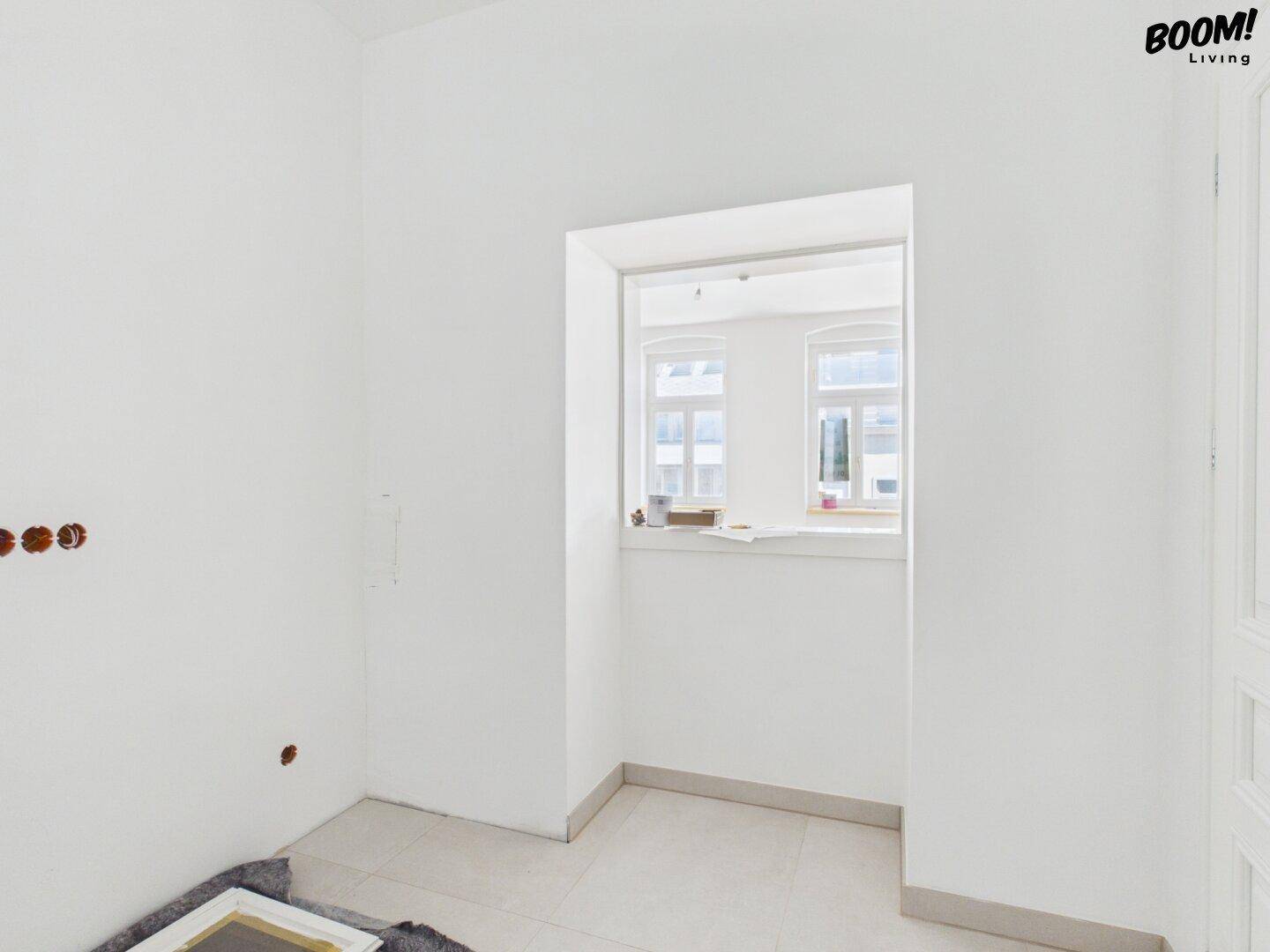 Kleiner, heller Raum mit Fliesenboden und Durchgang zu einem Fensterbereich.