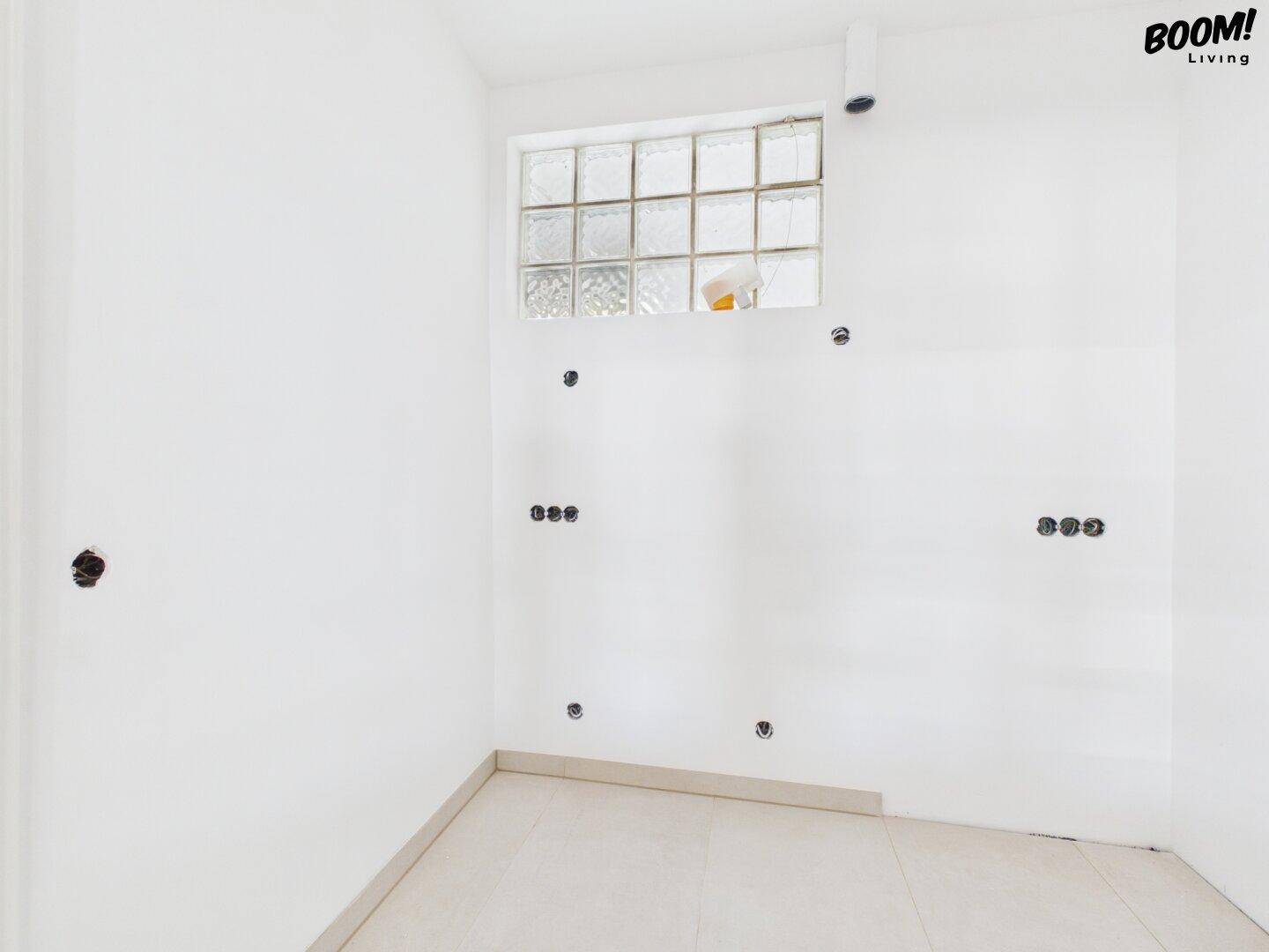 Leerer Raum mit Fliesenboden, Glasbausteinfenster und vorbereiteten Elektroinstallationen.