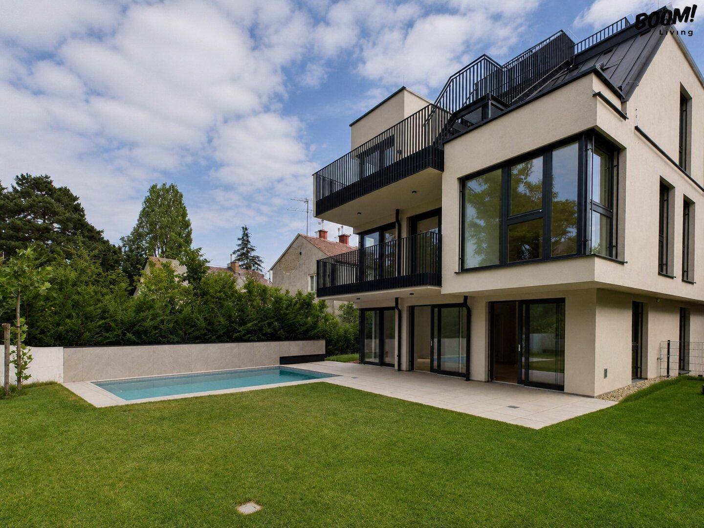 Rückansicht des modernen Wohnhauses mit gepflegtem Rasen, Pool und großzügiger Terrasse.