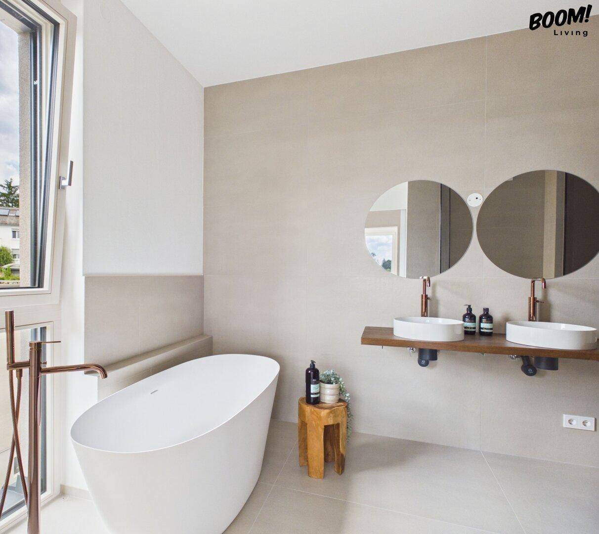 Luxuriöses Badezimmer mit freistehender Badewanne, Doppelwaschbecken und großen Fenstern.