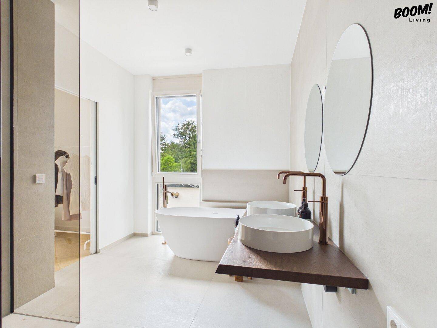 Helles Badezimmer mit freistehender Badewanne, Doppelwaschbecken und großem Fenster.
