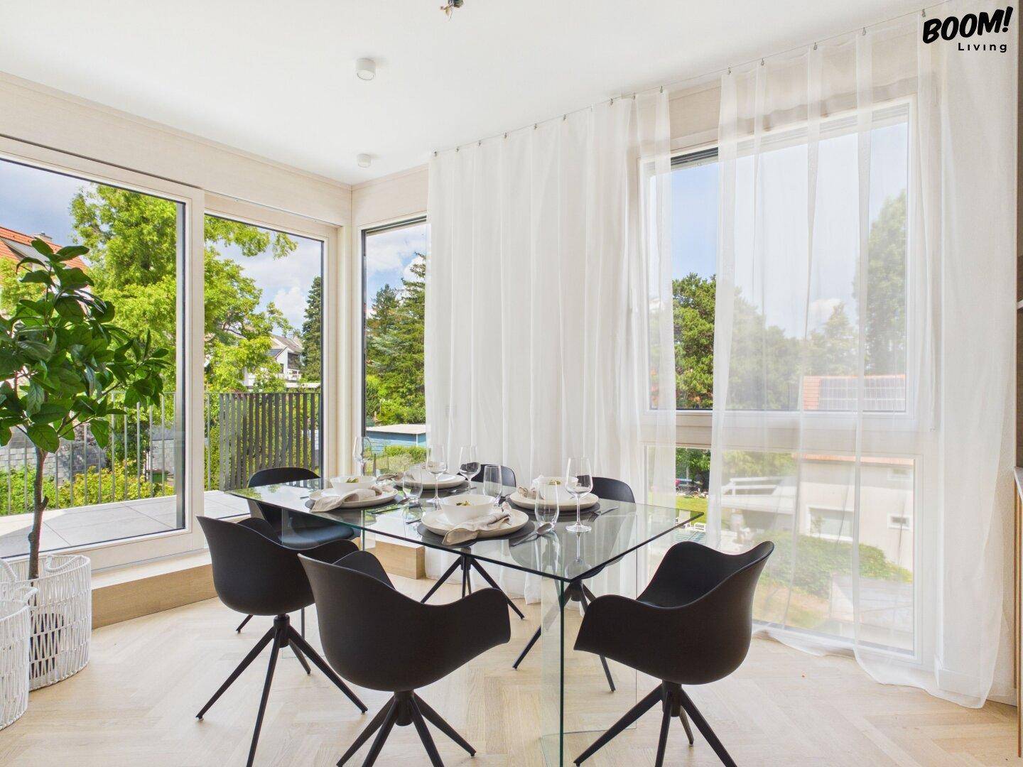 Eleganter Essbereich mit Glasstisch, modernen Stühlen und großen Fenstern mit Blick ins Grüne.