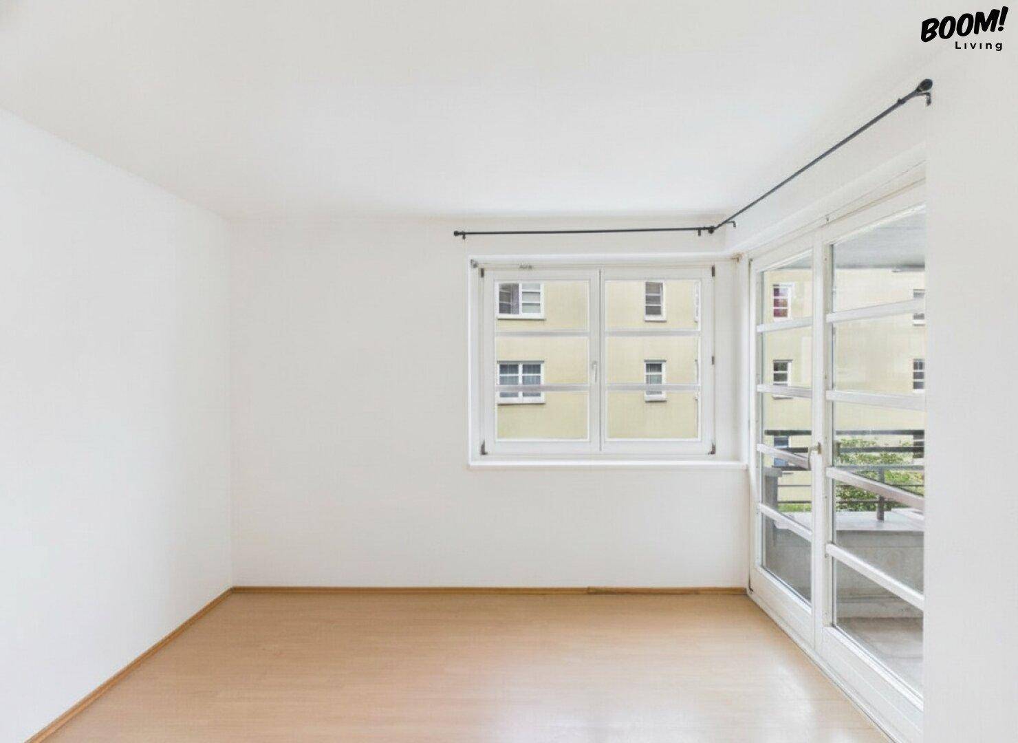 Heller, leerer Raum mit Fenster und Zugang zu einem Außenbereich.
