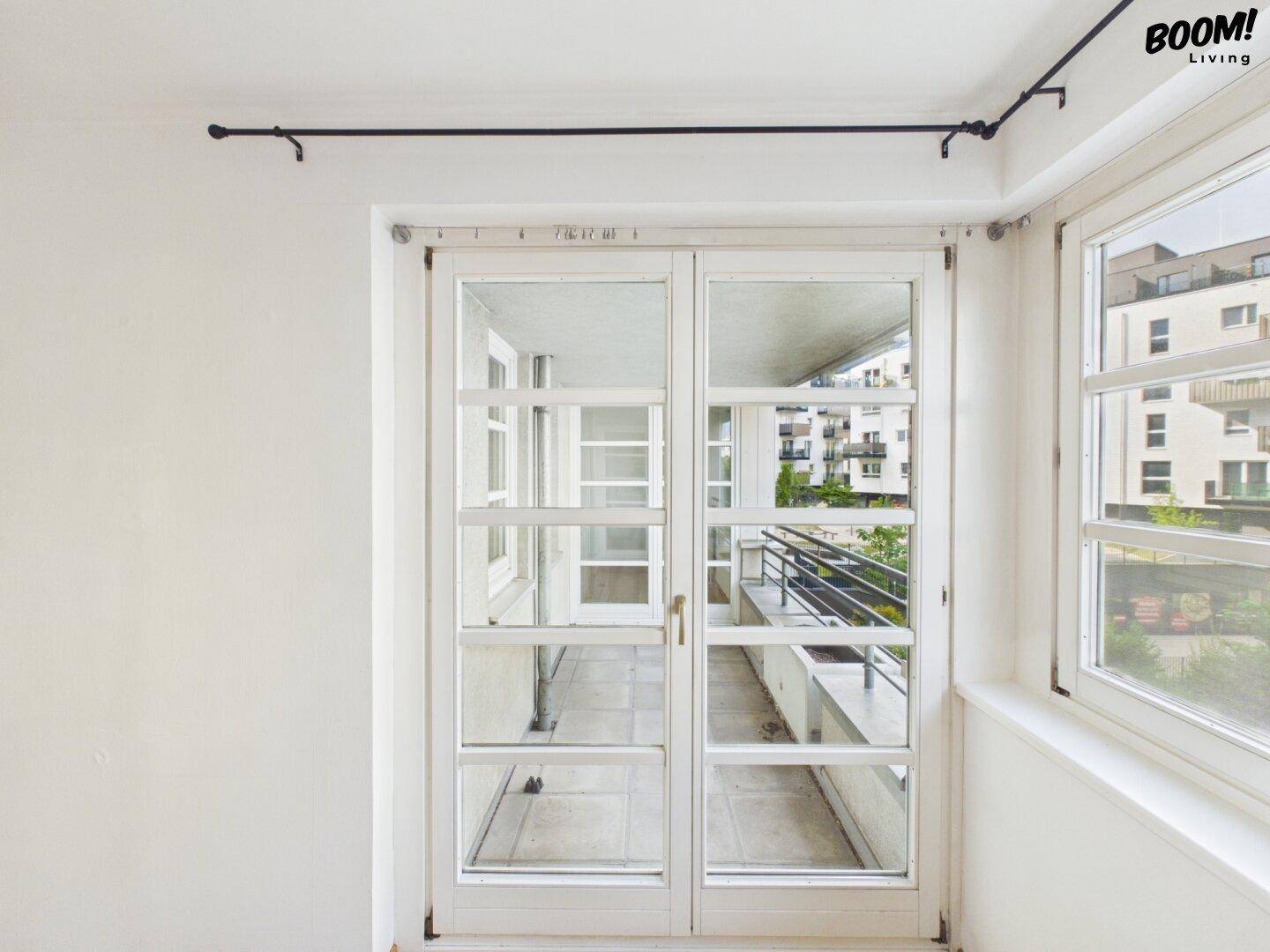 Heller Raum mit geschlossenen Türen, die zu einem verglasten Balkon führen.