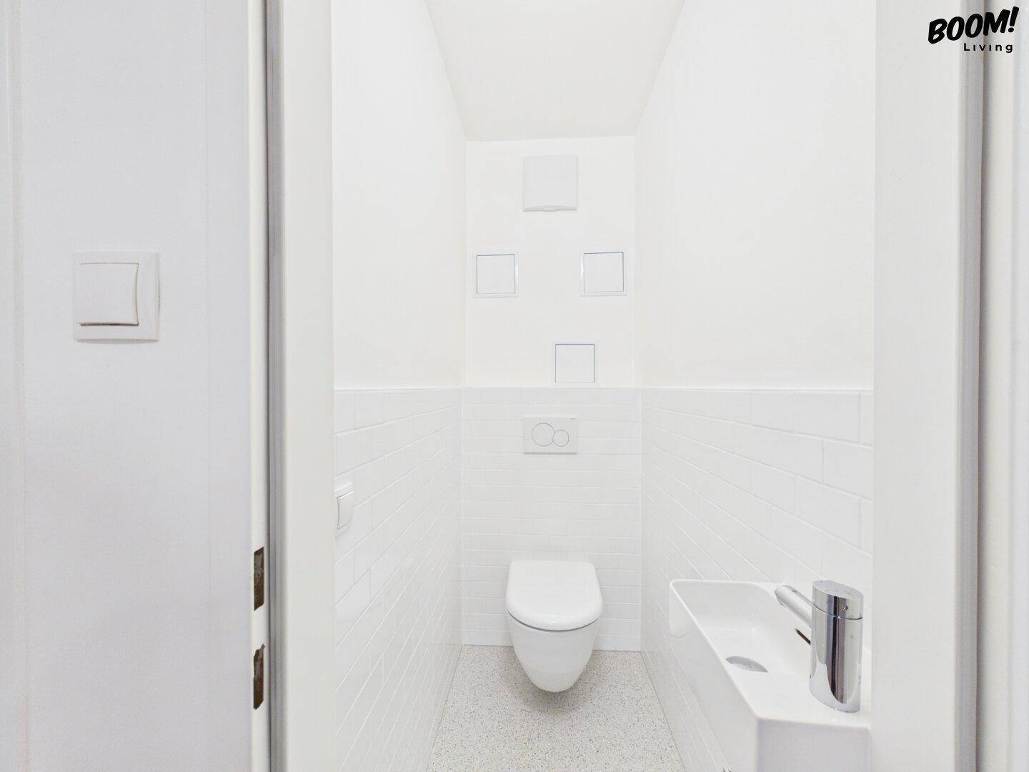 Modernes Gäste-WC mit wandhängender Toilette, kleinem Waschbecken und weißen Fliesen.