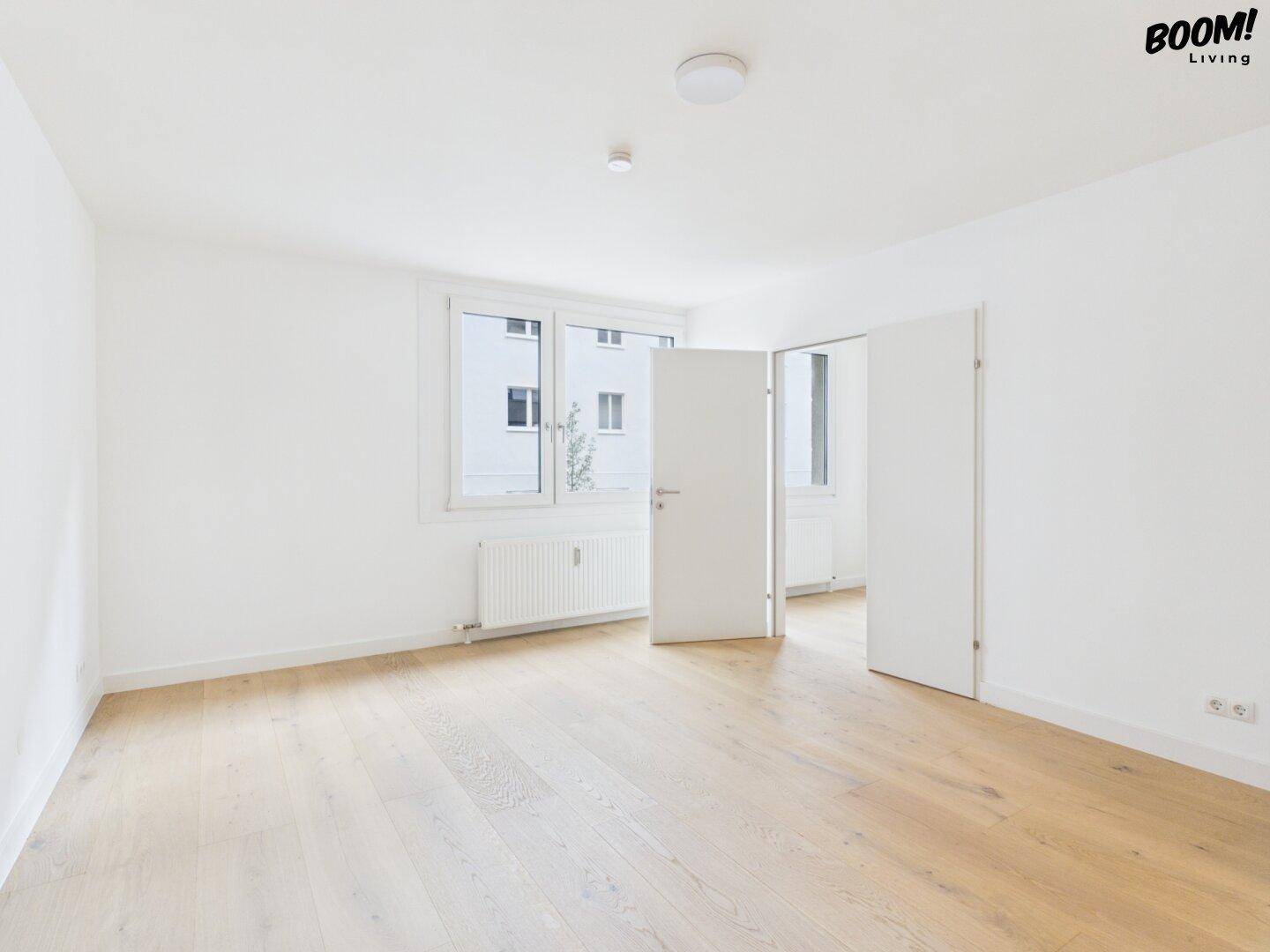 Helles, leeres Zimmer mit Parkettboden und großen Fenstern, das viel natürliches Licht hereinlässt.