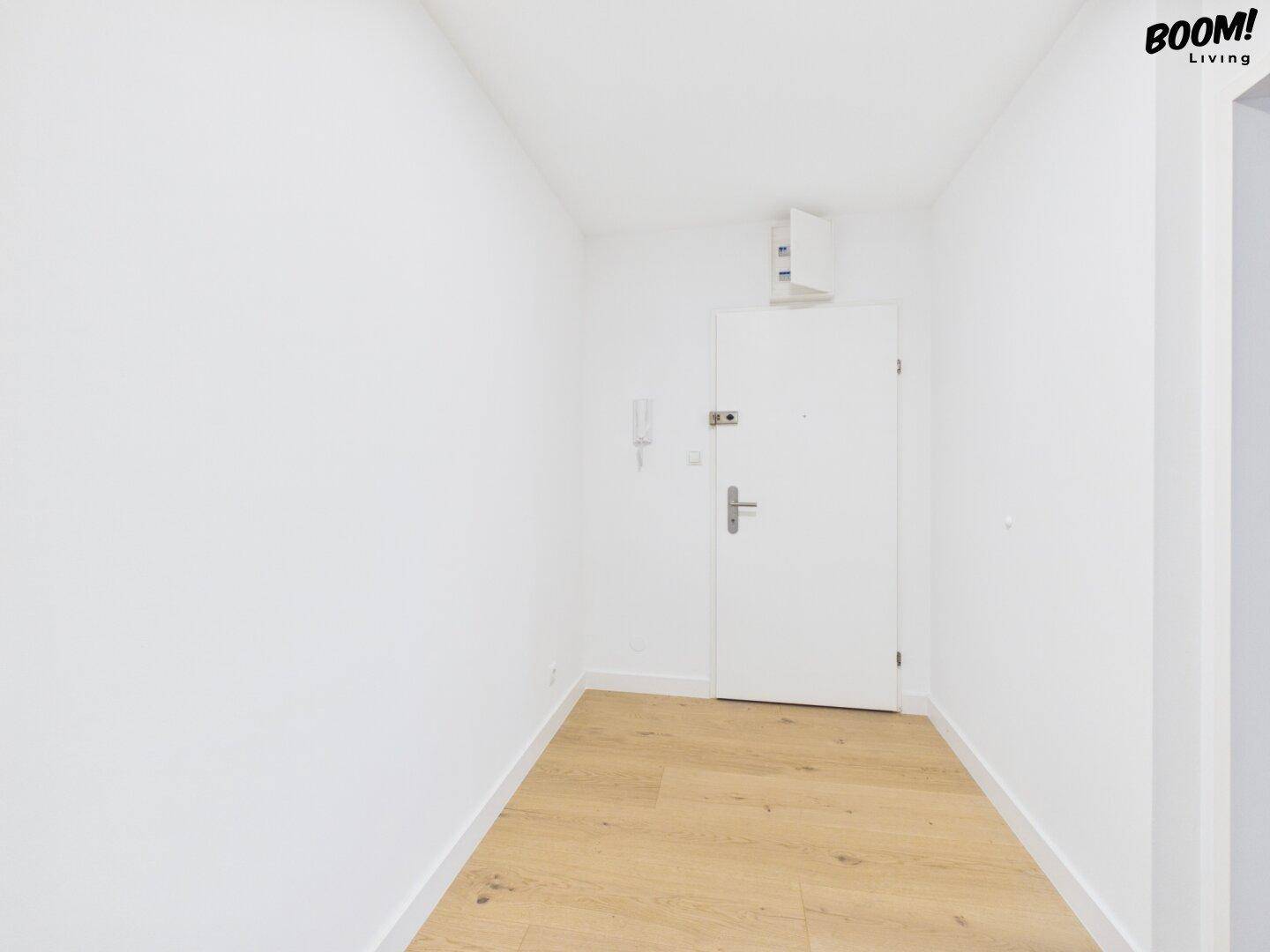 Heller Eingangsbereich mit Parkettboden, weißer Tür und Gegensprechanlage, der in die Wohnung führt.
