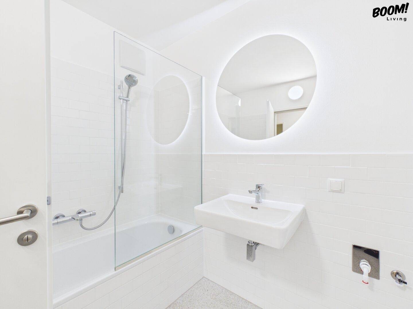 Modernes Badezimmer mit Badewanne, Duschabtrennung, Waschbecken und beleuchtetem Rundspiegel.