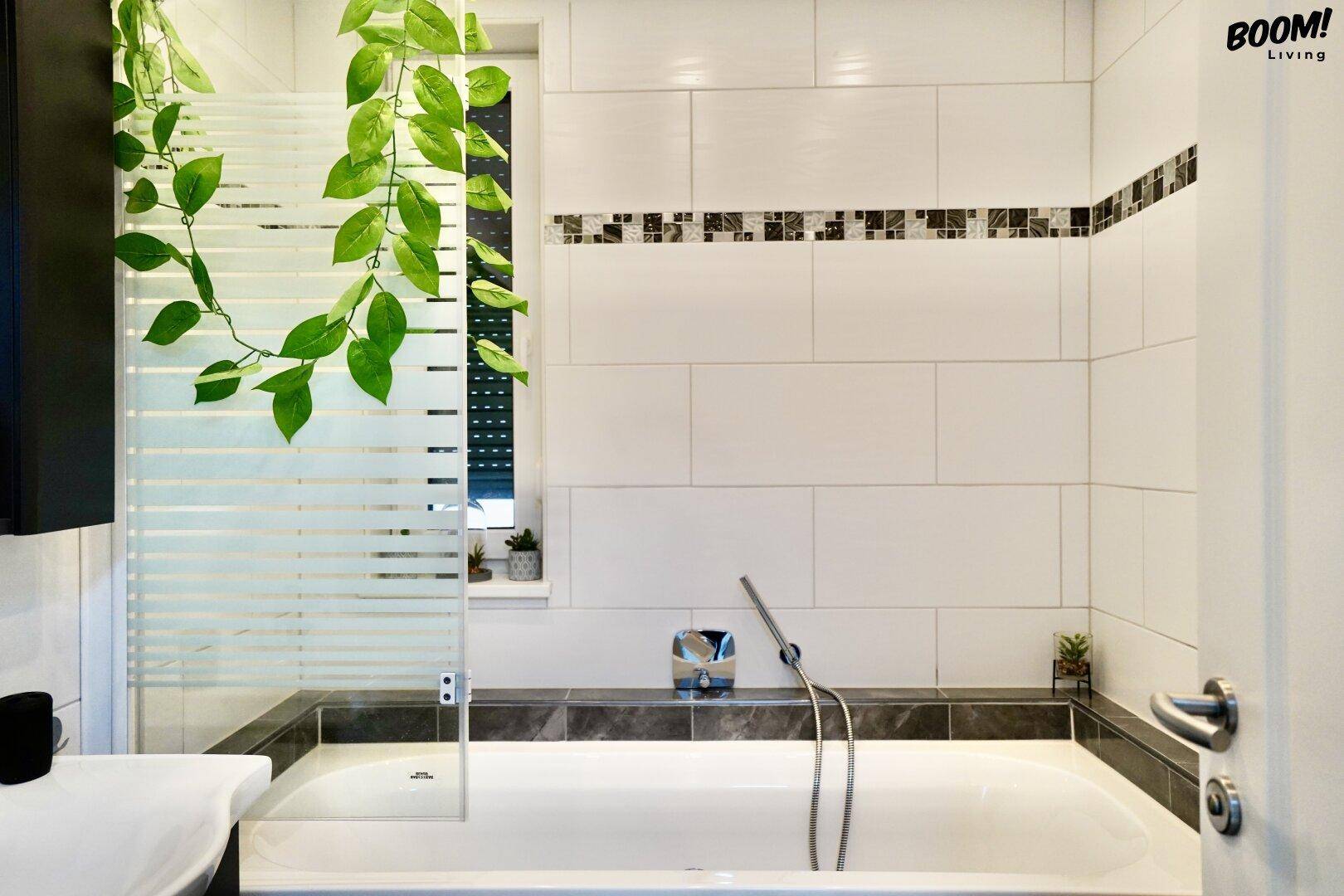 Helles Badezimmer mit Badewanne, weißen Fliesen und einer Glasabtrennung für die Dusche.