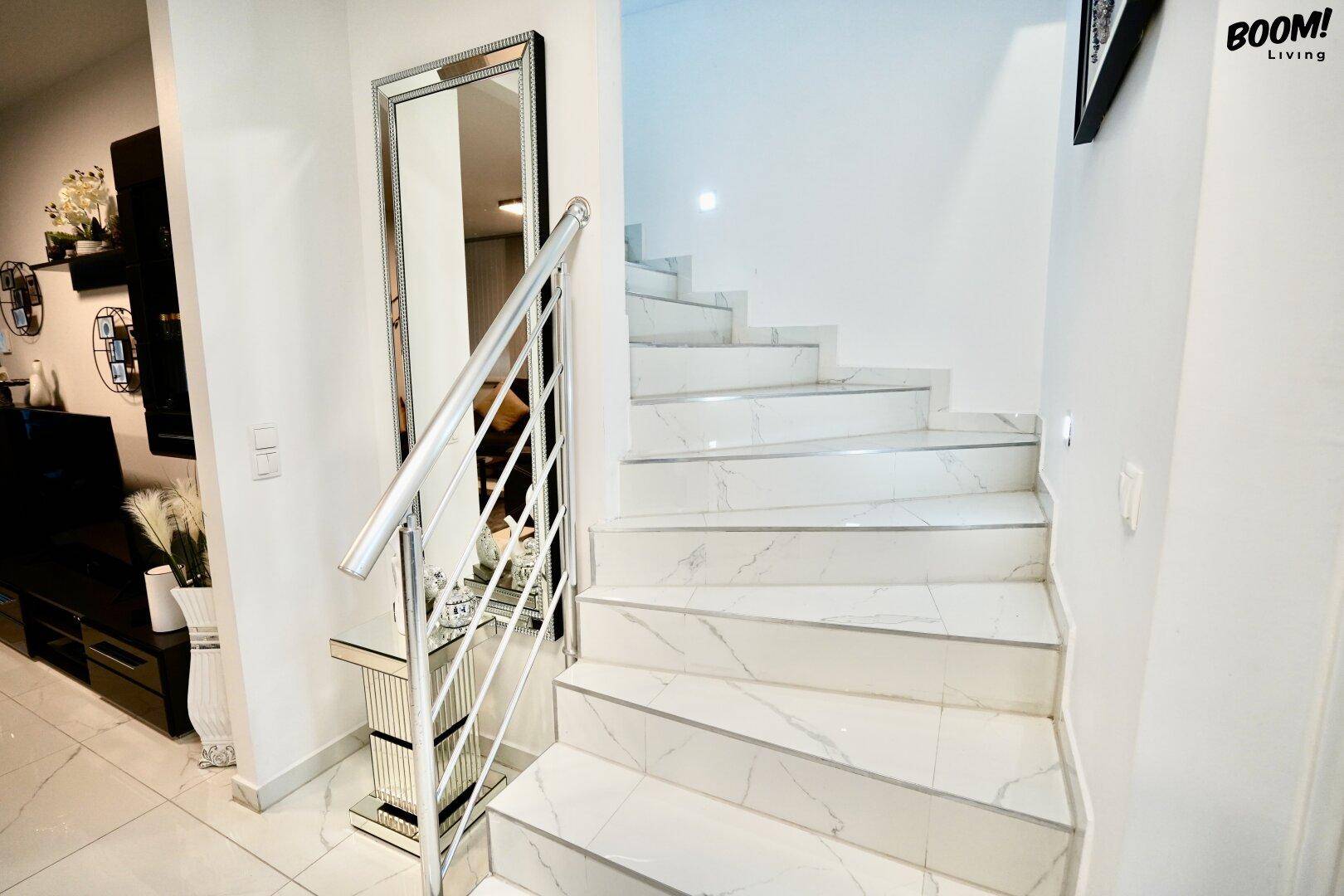 Elegante Treppe mit weißen Marmorstufen und modernem Metallgeländer, die die Etagen verbindet.