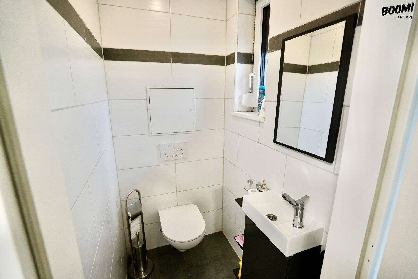 Kleines, hell gefliestes Gäste-WC mit wandhängendem WC, kleinem Waschbecken und Spiegel.