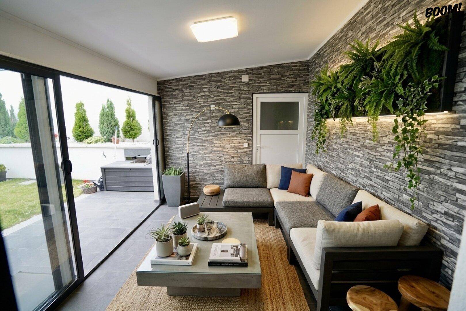 Gemütlicher Wintergarten mit L-förmigem Sofa, Steinfassade und großen Glasschiebetüren zum Garten.