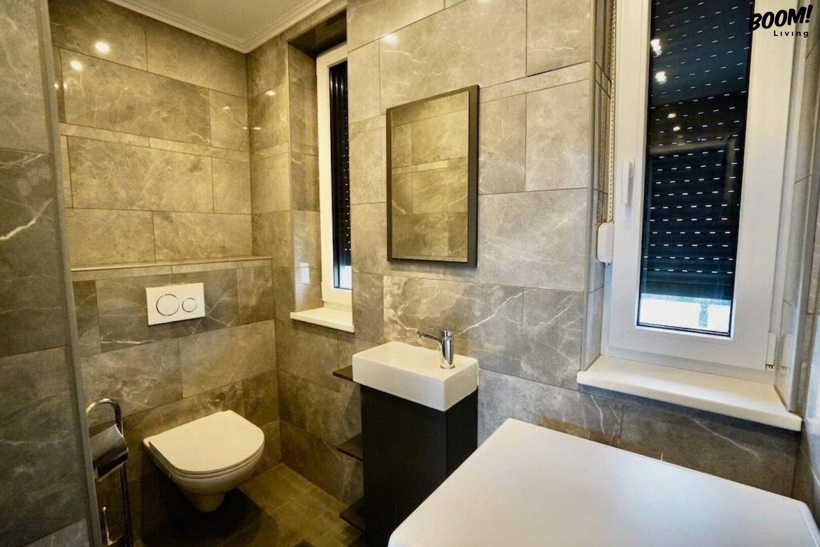 Modernes Gäste-WC mit grauen Marmorfliesen, wandhängendem WC und kleinem Waschbecken.