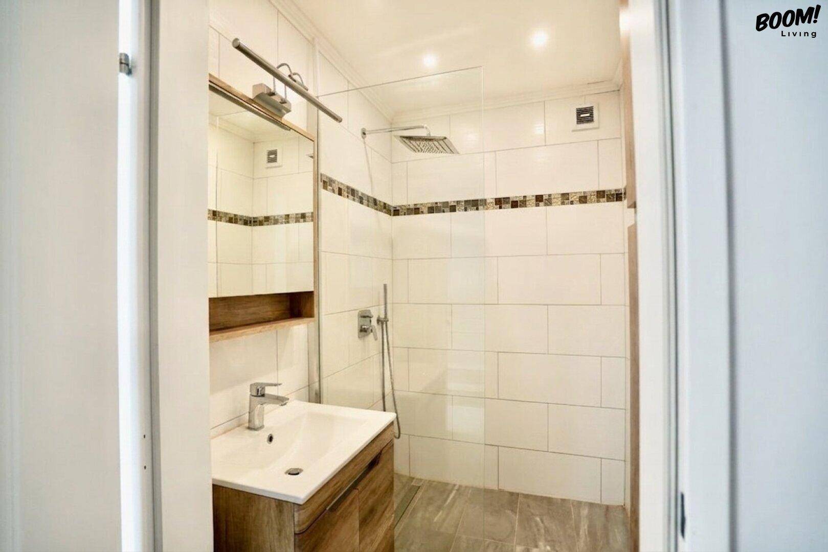 Modernes Badezimmer mit begehbarer Dusche, weißen Fliesen und einem Holzwaschtisch.