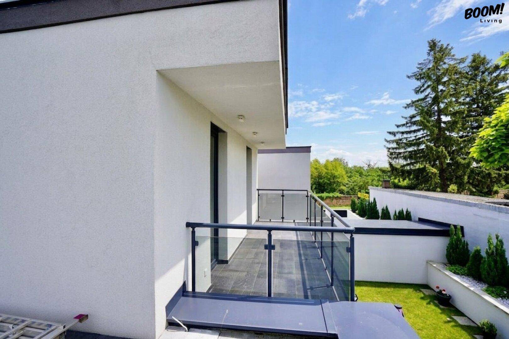 Balkon mit modernem Glasgeländer und Blick auf grüne Bäume und die Umgebung.
